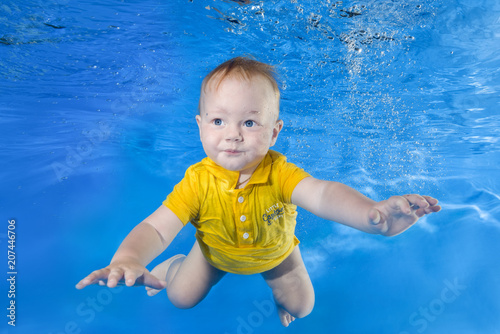 little boy in a yellow shirt learns to swim underwater in the pool