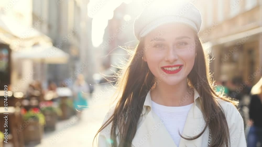 front view of walking smiling woman looking at camera on city street wind blowing long brunette hair sunny day warm bright sunshine on background bokeh flare sunrise scenery view happy girl portrait front view of walking smiling woman looking at camera on city street wind blowing long brunette hair sunny day warm bright sunshine on background bokeh flare sunrise scenery view happy girl portrait