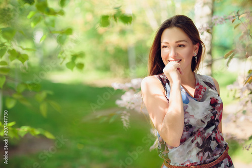 Young woman enjoying spring in the green field with blooming trees
