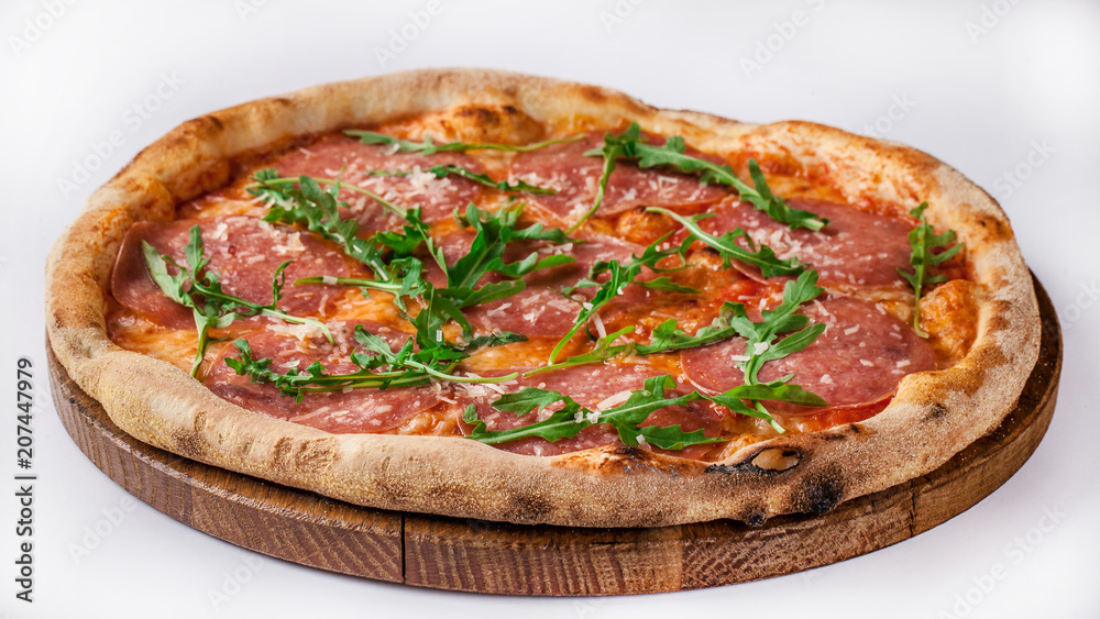 Italian pizza with ham, parma, arugula, parmesan, mozzarella lies on a wooden round board, on a white background