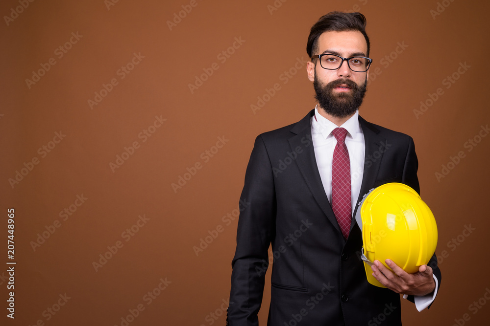 Young handsome bearded Persian businessman against brown backgro Young handsome bearded Persian businessman against brown backgro
