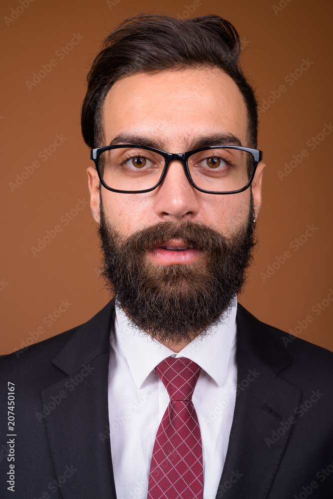 Young handsome bearded Persian businessman against brown backgro Young handsome bearded Persian businessman against brown backgro