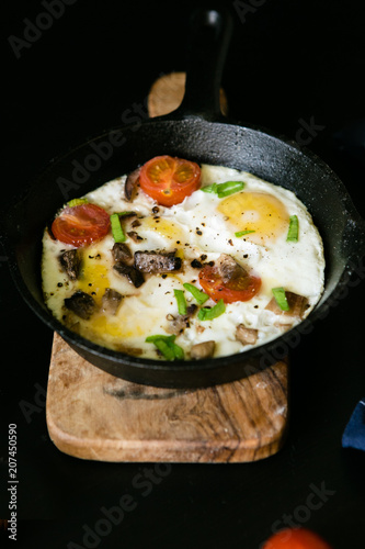 Scrambled eggs with vegetables and mushrooms in a cast-iron frying pan on a black background