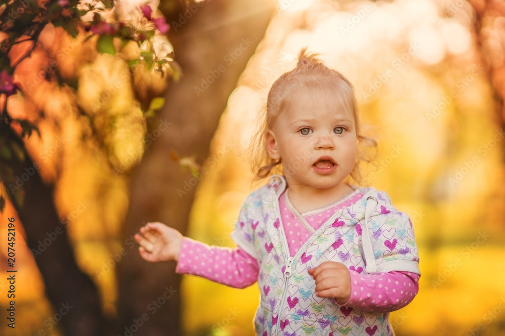 Little cute and cheerful baby girl, blonde girl, walking in a Sunny garden.