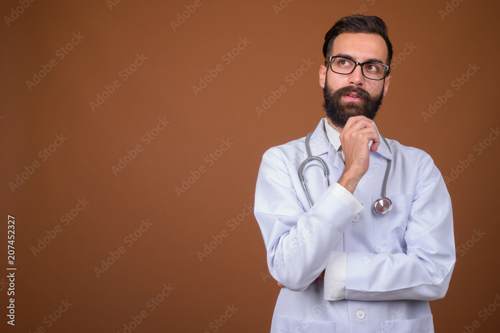 Young handsome bearded Persian man doctor against brown backgrou