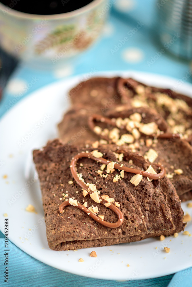 Chocolate oat pancakes with caramel and nuts with cup of coffee on blue fabric and grey wooden table. Chocolate oat pancakes with caramel and nuts with cup of coffee on blue fabric and grey wooden table.