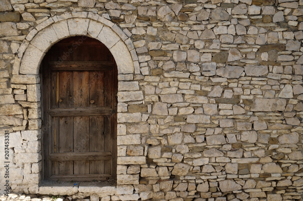 Stone wall with old wooden door in Old town Berat, Albania 