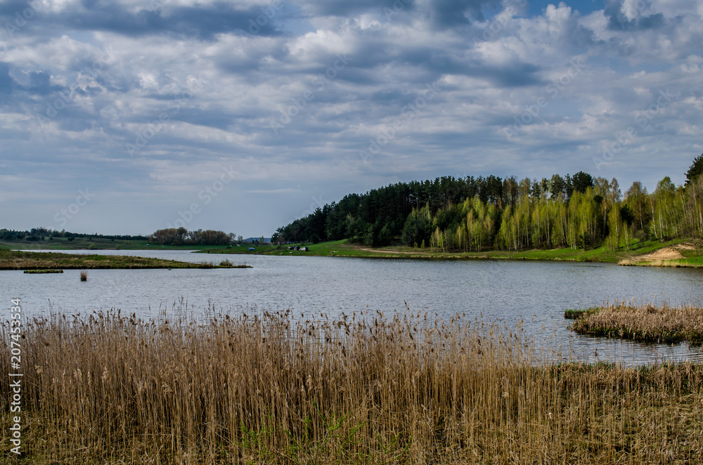 The large lake for fishing next to the forest. More clouds over the lake