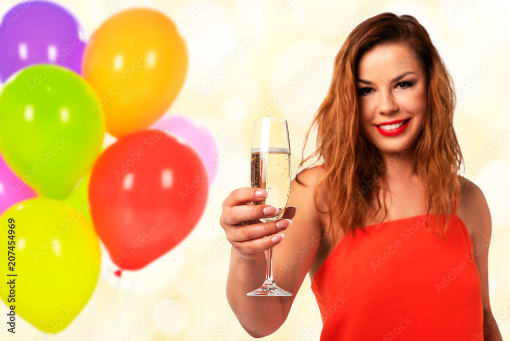 Celebration event concept - young and attractive woman in a red dress with perfect fingernails holds a glass of champagne or wine and smiling on a party decoration background (mixed). Celebration event concept - young and attractive woman in a red dress with perfect fingernails holds a glass of champagne or wine and smiling on a party decoration background (mixed).