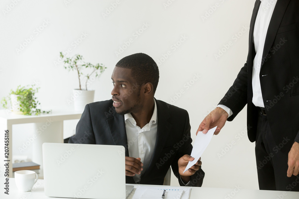 Person giving envelope with bribe to worried African American colleague, partners being corrupt in office making illegal deal, planning fraud, intriguing. Concept of corruption, unethical manipulation Person giving envelope with bribe to worried African American colleague, partners being corrupt in office making illegal deal, planning fraud, intriguing. Concept of corruption, unethical manipulation