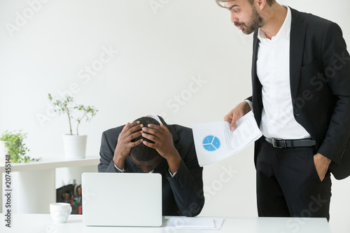 Mad Caucasian employer yelling at depressed African American worker, blaming for business failure and documents mistake, humiliating black subordinate. Concept of work discrimination, demonization photo