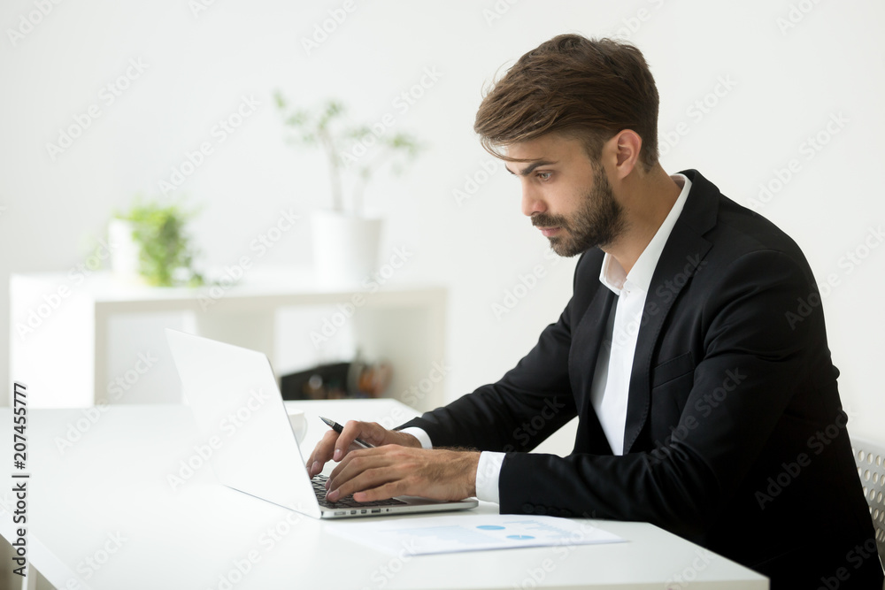 Serious Caucasian businessman wearing formal wear working at laptop typing, answering to business partner, writing email at computer, browsing internet searching for information. Concept of technology Serious Caucasian businessman wearing formal wear working at laptop typing, answering to business partner, writing email at computer, browsing internet searching for information. Concept of technology