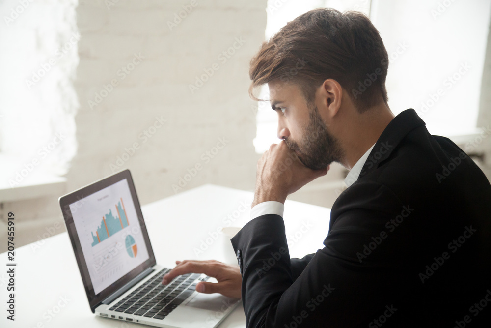 Serious thoughtful businessman looking at laptop screen, thinking about rates and sales growth, company successful strategy, analyzing financial statistics, solving business problem Serious thoughtful businessman looking at laptop screen, thinking about rates and sales growth, company successful strategy, analyzing financial statistics, solving business problem