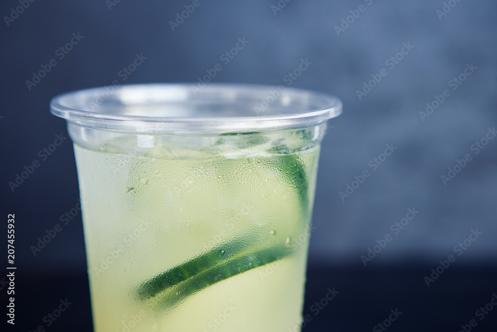 Cold cucumber lemonade in the plastic cup on the black background Cold cucumber lemonade in the plastic cup on the black background