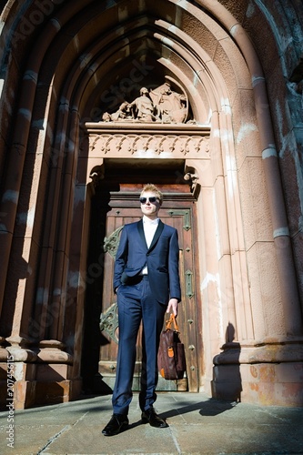 stylish handsome young man in sunglasses and suit near the entrance of old building