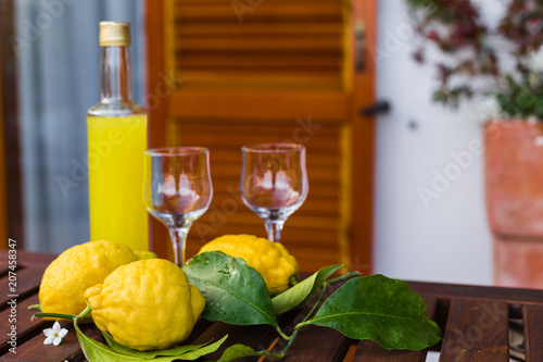 Lemonade or limoncello in a glass bottle, glasses, lemons with leaves on a serving table on the terrace