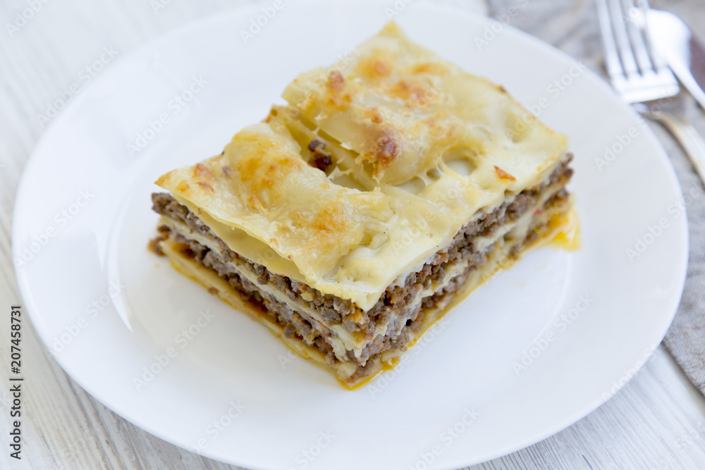 Delicious beef lasagne served on a white round plate, white wooden background. Side view. Delicious beef lasagne served on a white round plate, white wooden background. Side view.