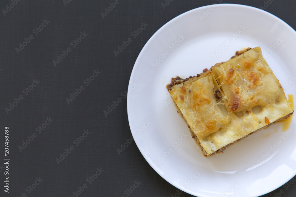 Traditional beef lasagne on a white round plate, dark background, top view. Flat lay, from above. Copy space.