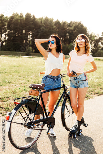 Two beautiful sexy girls, hipsters, modern style, ride a bike and roller  skates, and drink soda through the straws, Summer time, fun, sunset in  nature Stock-foto | Adobe Stock