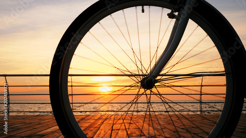 Spinning bicycle wheel against amazing sunrise and sea. Close up bike truck rotating with sky background
