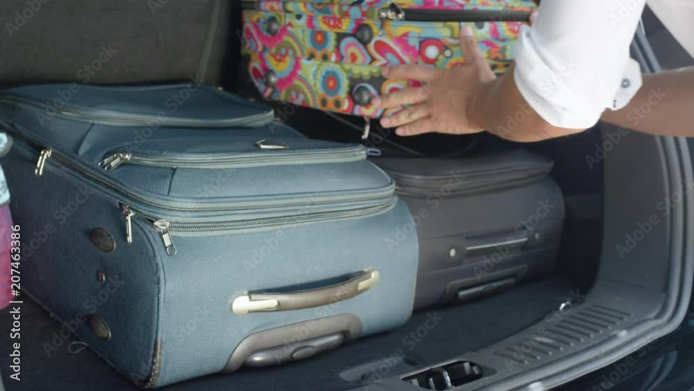 SLOW MOTION, CLOSE UP: Unrecognizable male tourist packing his and his girlfriend's bags in the back of a spacious black car. Unknown man putting baggage in black car parked in the sunny driveway.