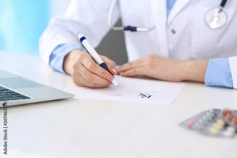 Female doctor filling up prescription form while sitting at the desk in hospital closeup. Healthcare, insurance and excellent service in medicine concept Female doctor filling up prescription form while sitting at the desk in hospital closeup. Healthcare, insurance and excellent service in medicine concept