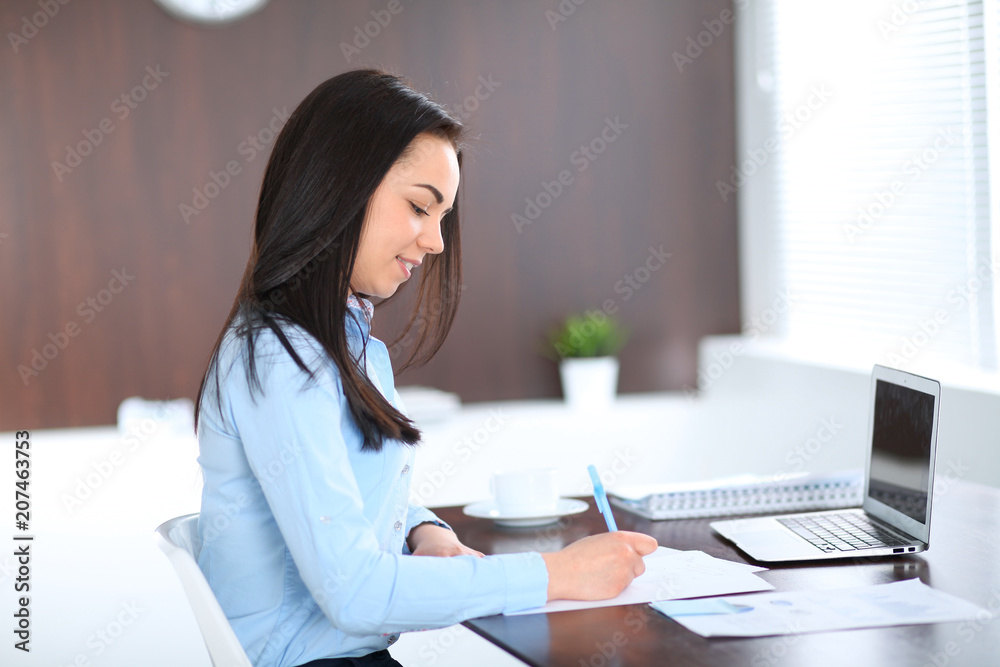 Young brunette business woman looks like a student girl working in office. Hispanic or latin american girl sitting at the desk with laptop computer