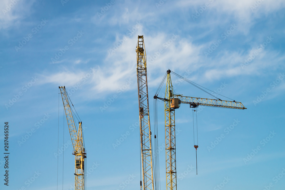 Big tower cranes against the blue sky. Background image of construction equipment close-up with copy space. Build of city. Big tower cranes against the blue sky. Background image of construction equipment close-up with copy space. Build of city.