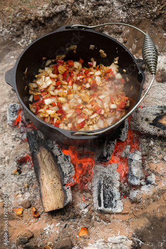 Vegetables cooking in a dutch oven sitting in a campfire outdoors