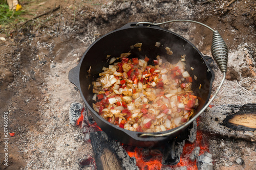 Vegetables cooking in a dutch oven sitting in a campfire outdoors
