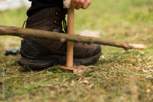 Woman using knife and dry materials with friction bow to start a fire in the forest