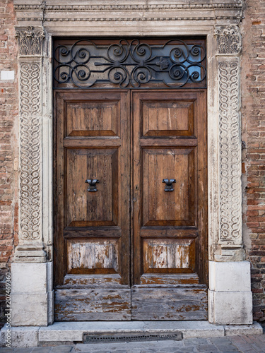 Old wooden portal with columns and architrave in white stone.