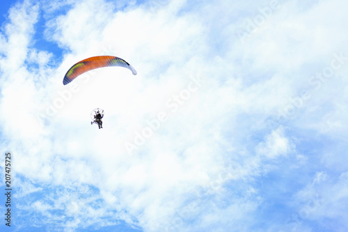 Paraglider flying in the blue sky against the background of clouds