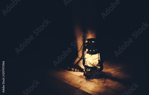 Girl legs on a wooden floor under the light from a oil lamp in the dark.