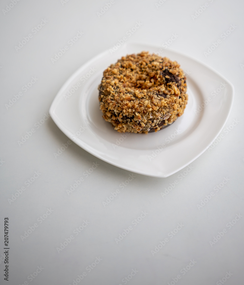Single ground peanut coated on chocolate flour donut on white plate isolated on white Single ground peanut coated on chocolate flour donut on white plate isolated on white