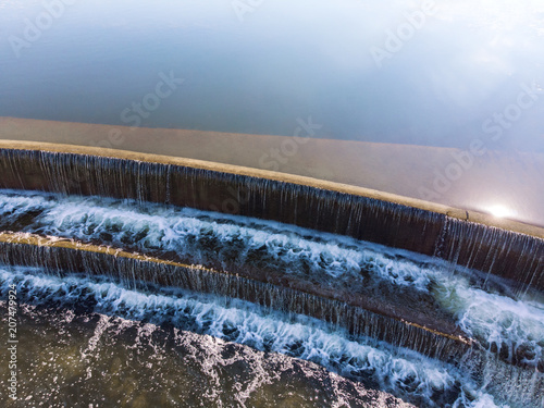 summer background with water flowing down. sun and blue sky reflect in water. urban waterfall. aerial view