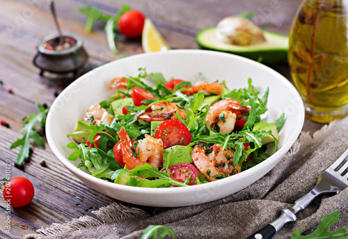 Fresh salad bowl with shrimp, tomato, avocado and arugula on wooden background close up. Healthy food. Clean eating.