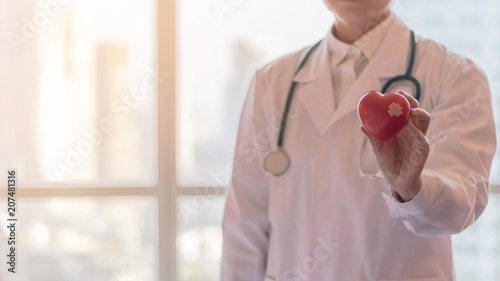Cardiologist doctor holding red heart in clinical hospital for medical healthcare concept