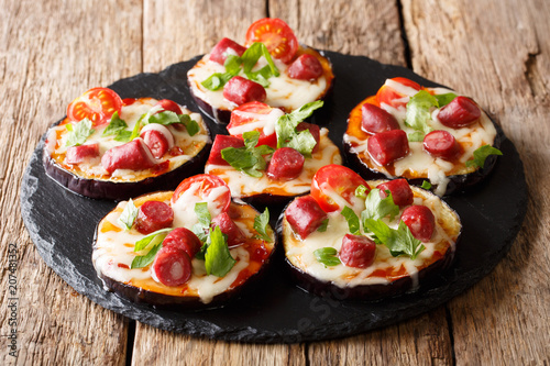 light snack from hot eggplants with cheese, tomatoes, sausages and sauce close-up on the table. horizontal