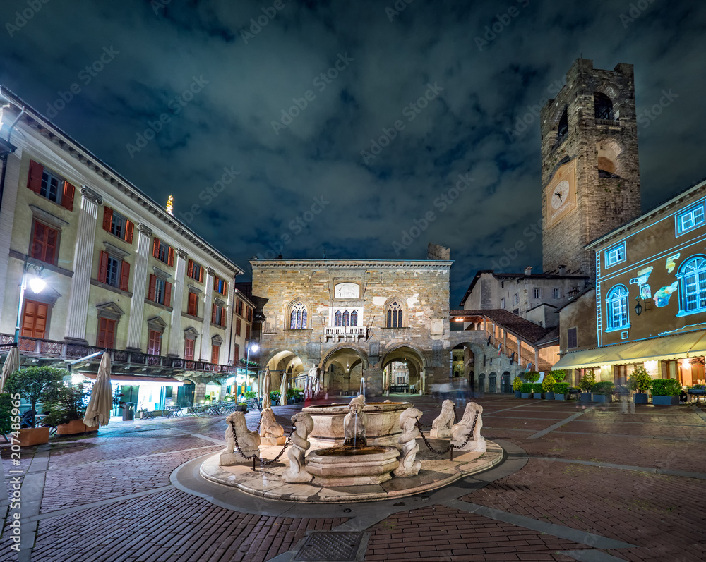 Contarini fountain on Piazza Vecchia square and Campanone tower in the old part of Bergamo, Italy at night.