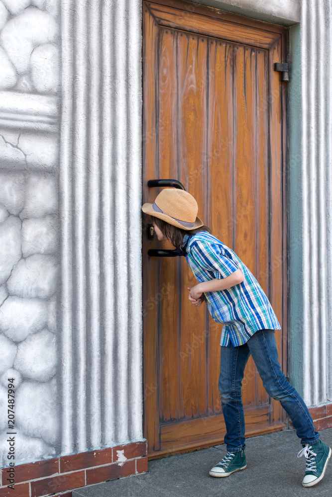 A schoolboy in a hat and tie - a butterfly is standing by a wooden door and looks in the keyhole A schoolboy in a hat and tie - a butterfly is standing by a wooden door and looks in the keyhole