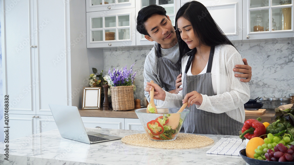 The couple are cooking together happily with laptop computer