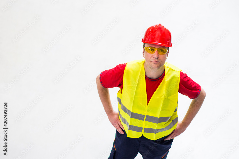Factory worker on white background looking up with arms on his hips. Worker wearing yellow reflective west, yellow safety glasses and red helmet Factory worker on white background looking up with arms on his hips. Worker wearing yellow reflective west, yellow safety glasses and red helmet