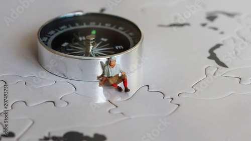 Tablou pe pânză Miniature man sitting beside a compass.