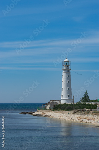 seascape with beautiful white lighthouse on blue sky background.