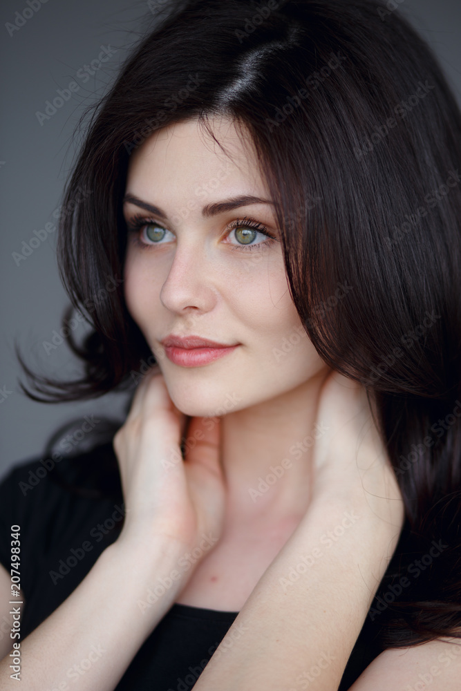 A sexy brunette with green eyes, wavy hair with volume,looks innocent and cute with hands . Vertical view on the gray background. A sexy brunette with green eyes, wavy hair with volume,looks innocent and cute with hands . Vertical view on the gray background.