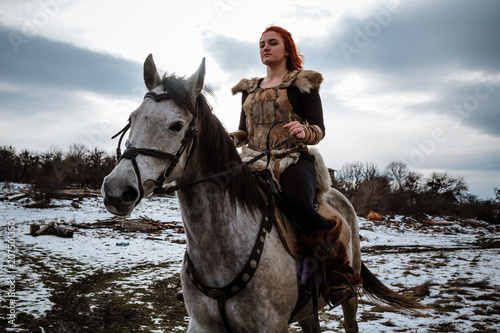 Beautiful girl on horse and with red hair in armor. Woman is a Viking. Fantasy