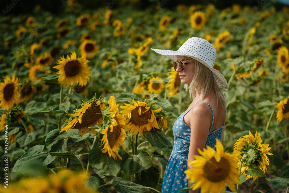 beautiful sweet sexy girl in a blue dress walking on a field of sunflowers , smiling a beautiful smile,cheerful girl,style, lifestyle , ideal for advertising and photo sun shines bright and juicy