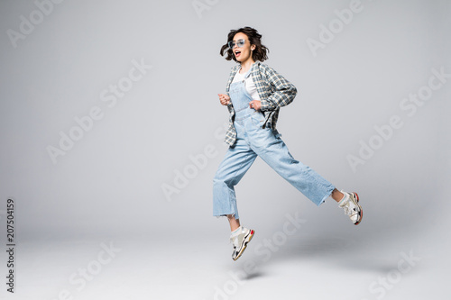 Full length of playful young woman gesturing and smiling while jumping against grey background