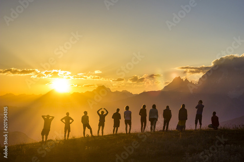 group of people with hands up standing on grass in sunset mountains